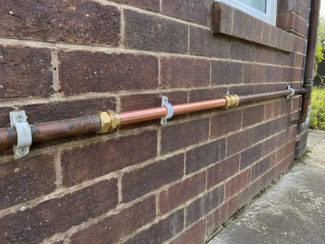 Repaired copper water pipe on a brick exterior wall beside a window in Neath